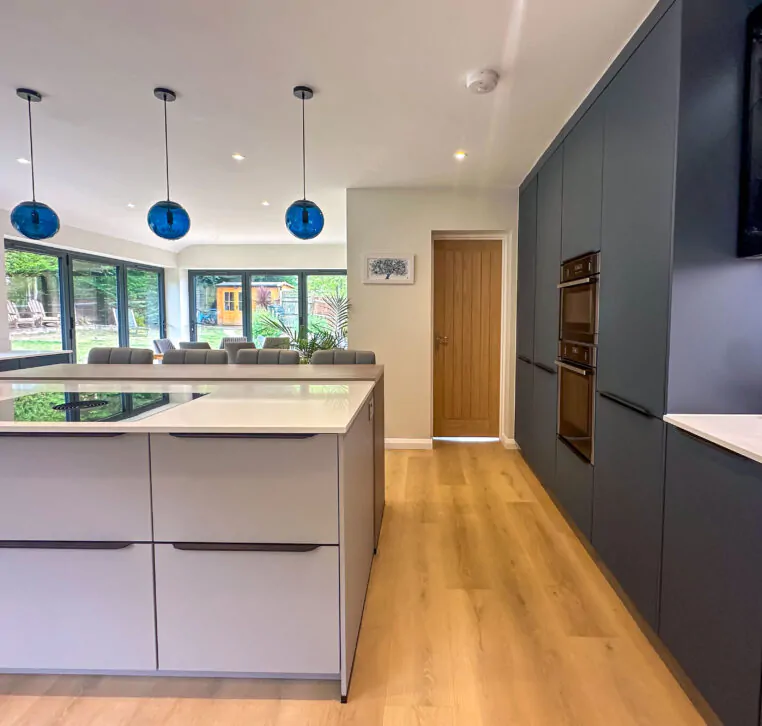 Spacious kitchen with light grey island, blue cabinets, and a view of the outdoor garden