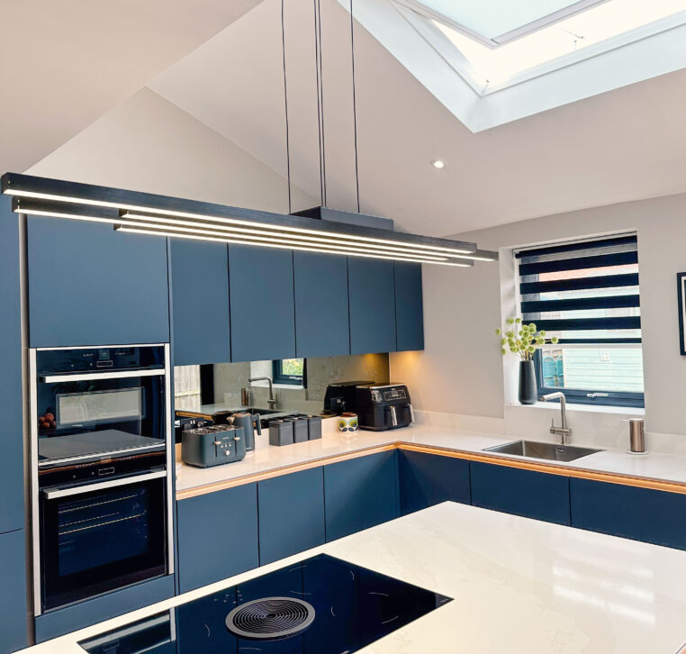 Image showing a modern kitchen with dark blue cabinetry, large island with induction hob, and skylights overhead.