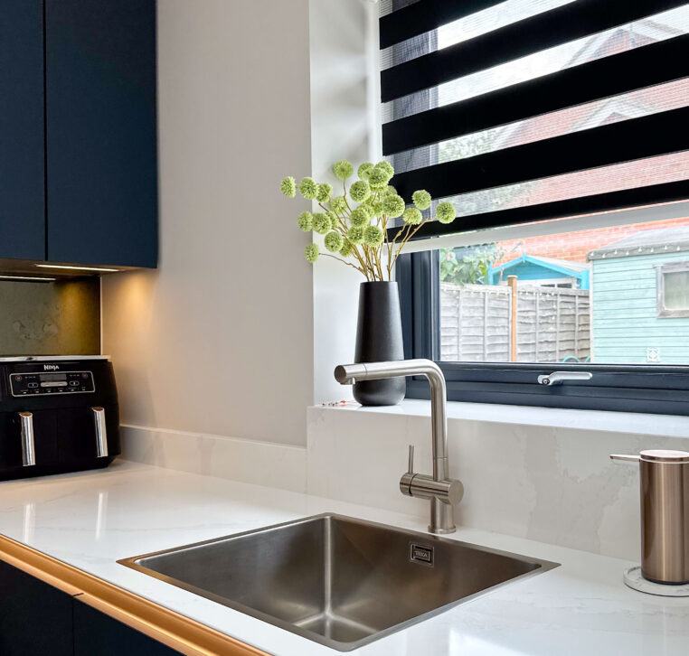 Close-up of the kitchen sink area with sleek faucet and quartz countertop, under a skylight.