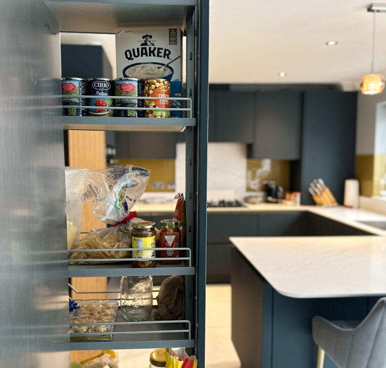Pull-out pantry storage in a modern kitchen with gold cabinets and Calacatta Gold quartz worktop.