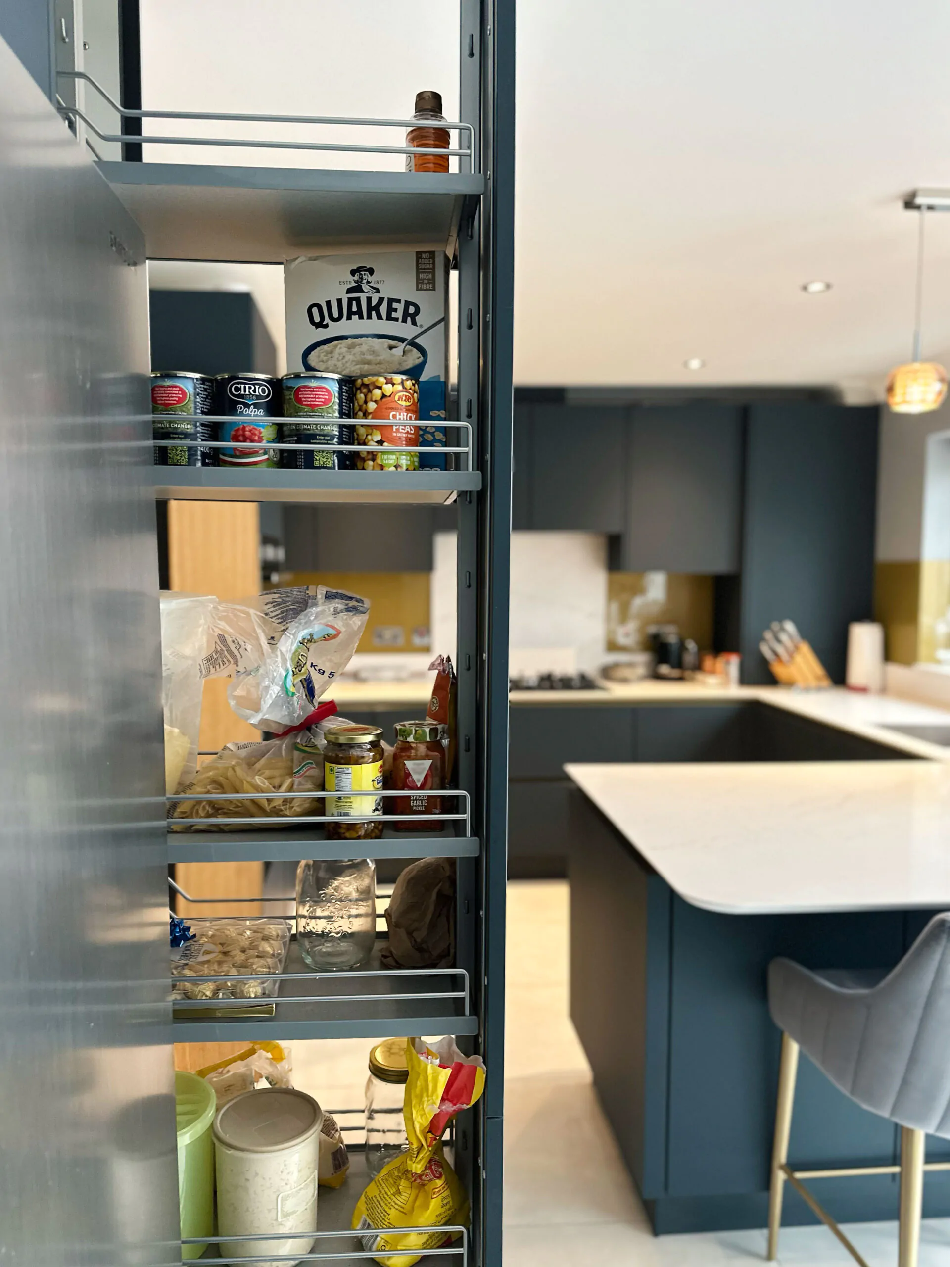 Pull-out pantry storage in a modern kitchen with gold cabinets and Calacatta Gold quartz worktop.