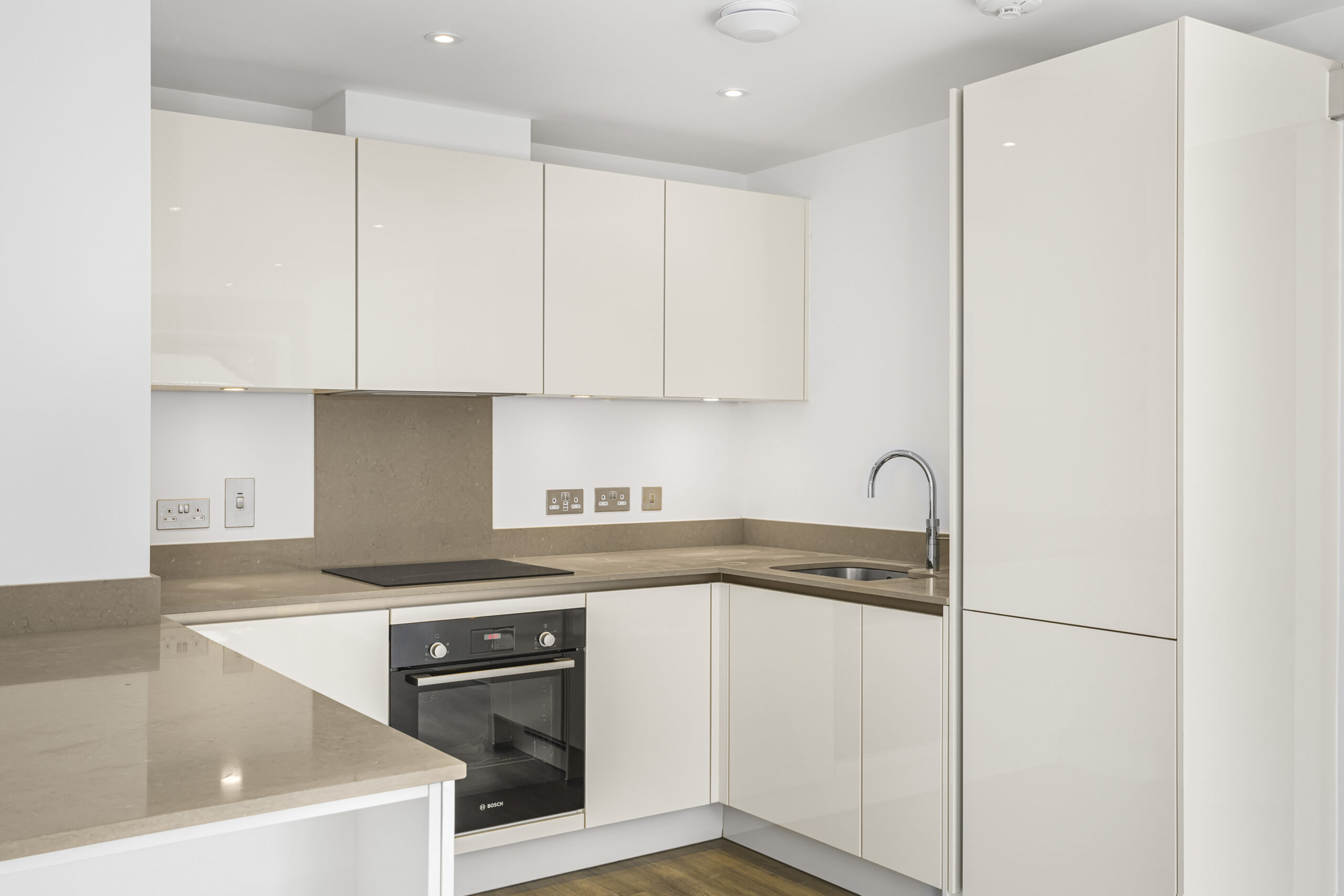 Modern white kitchen with built-in oven, minimalist design, and U-shaped layout in Reading new-build
