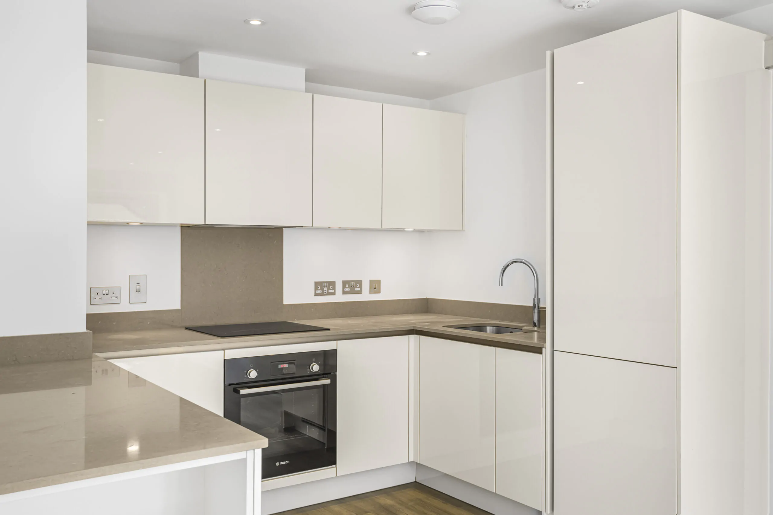 Modern white kitchen with built-in oven, minimalist design, and U-shaped layout in Reading new-build