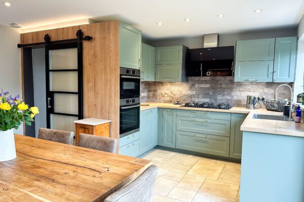 Modern kitchen view with integrated ovens, wood shaker cabinets, and rustic dining table