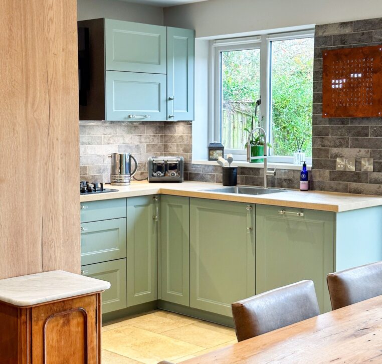 Corner layout of a U-shaped kitchen with green shaker cabinets and modern appliances