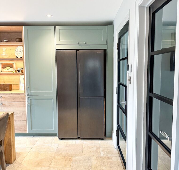 Close-up of light green wood shaker kitchen cabinets with grey brick backsplash