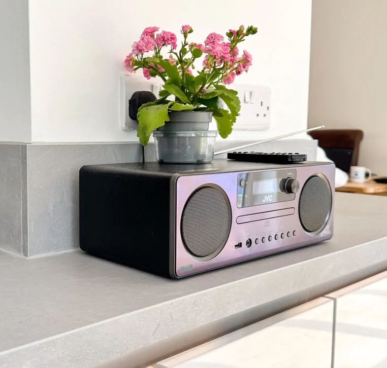Close-up of a grey kitchen worktop with a small radio and pink flowers in a pot