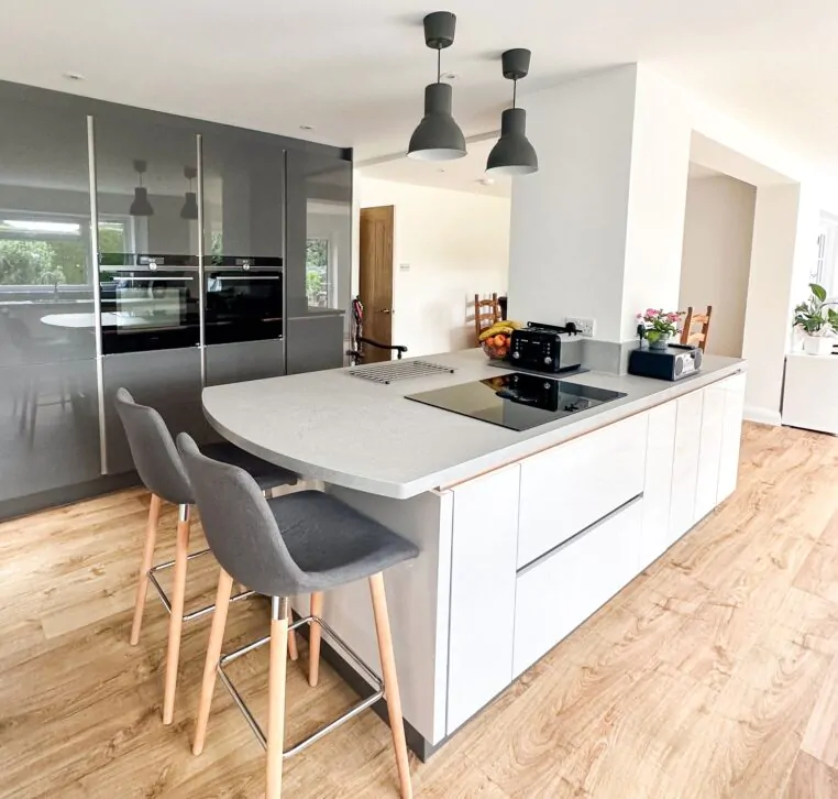 Modern kitchen view with grey high-gloss cabinets, ovens, and wooden flooring