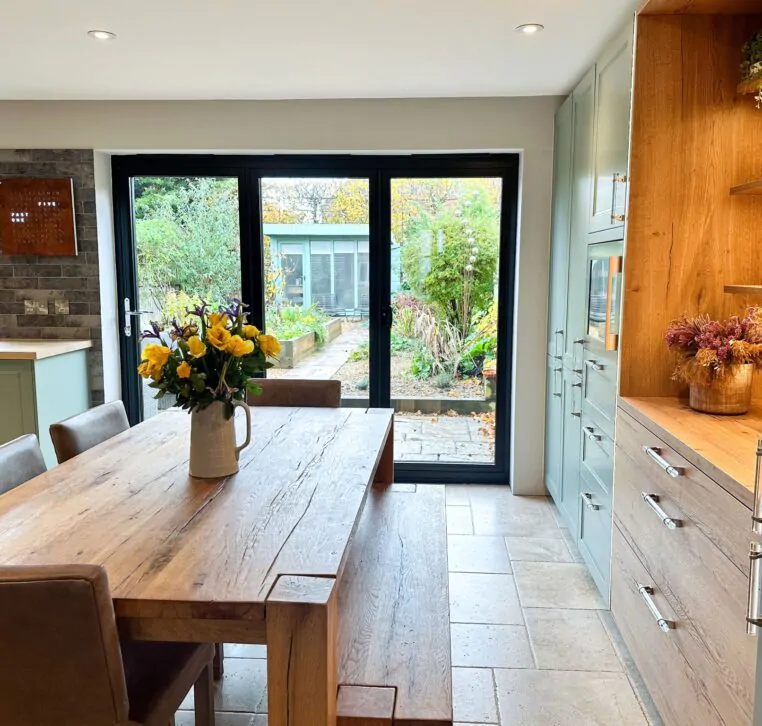 Elegant U-shaped wood shaker kitchen with green cabinets, wooden elements, and natural light