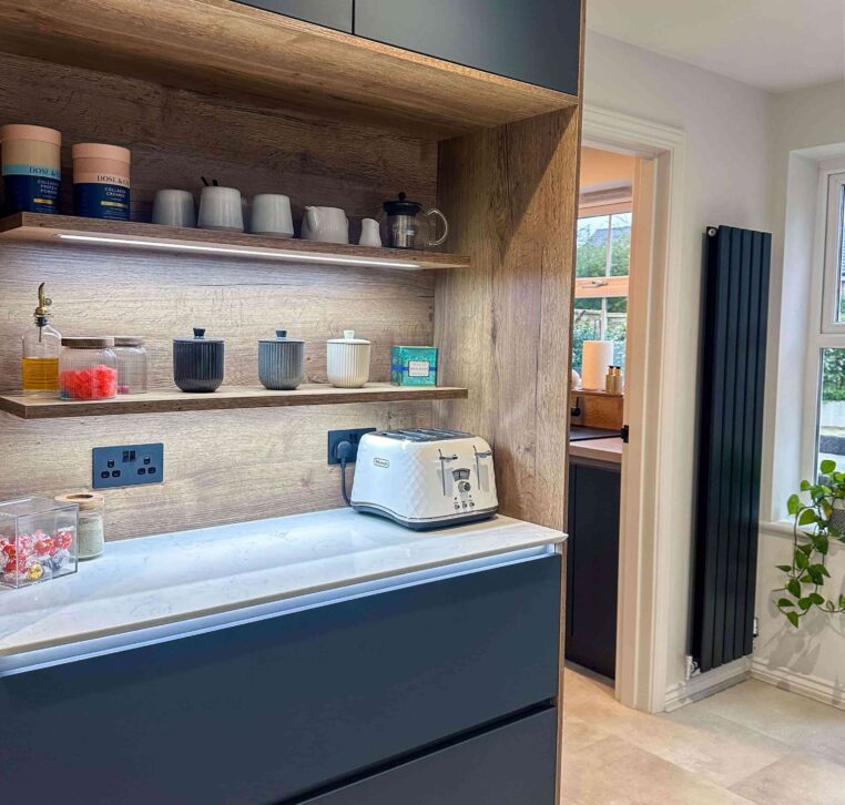 Built-in wooden kitchen shelving with under-cabinet lighting, featuring stylish jars, cups, and a white toaster