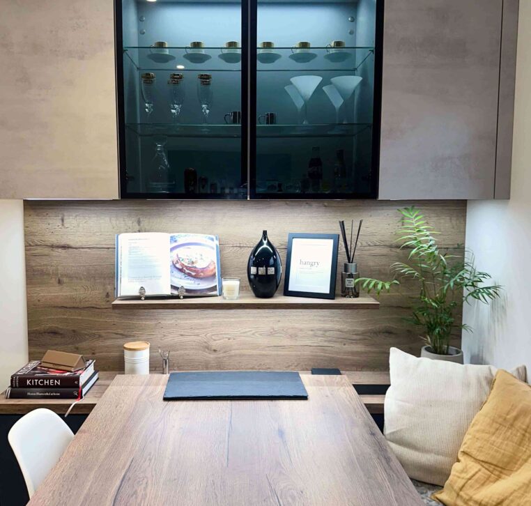 Elegant dining area with a wooden table, built-in shelving, and illuminated glass-fronted cabinets showcasing glassware