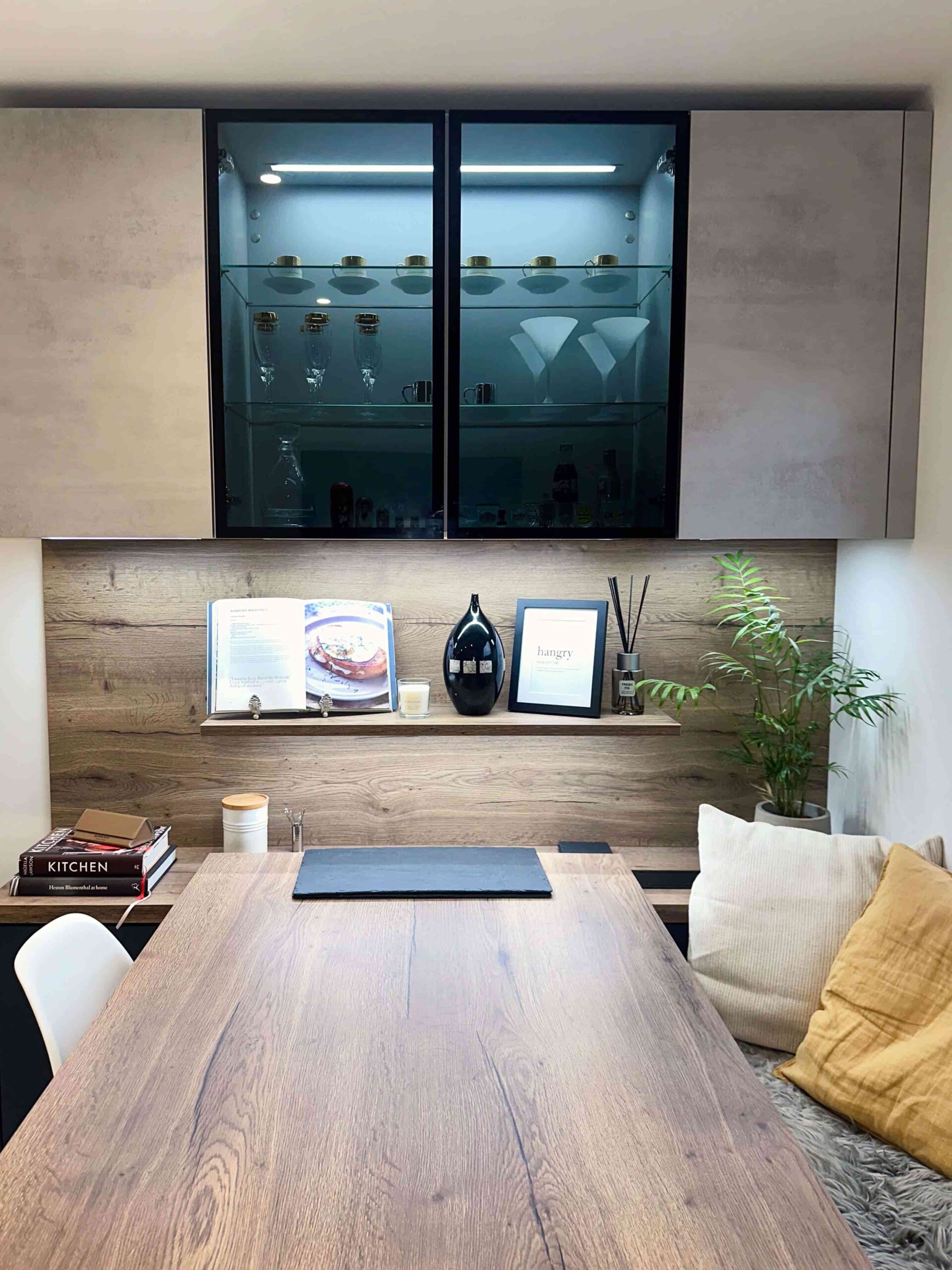 Elegant dining area with a wooden table, built-in shelving, and illuminated glass-fronted cabinets showcasing glassware