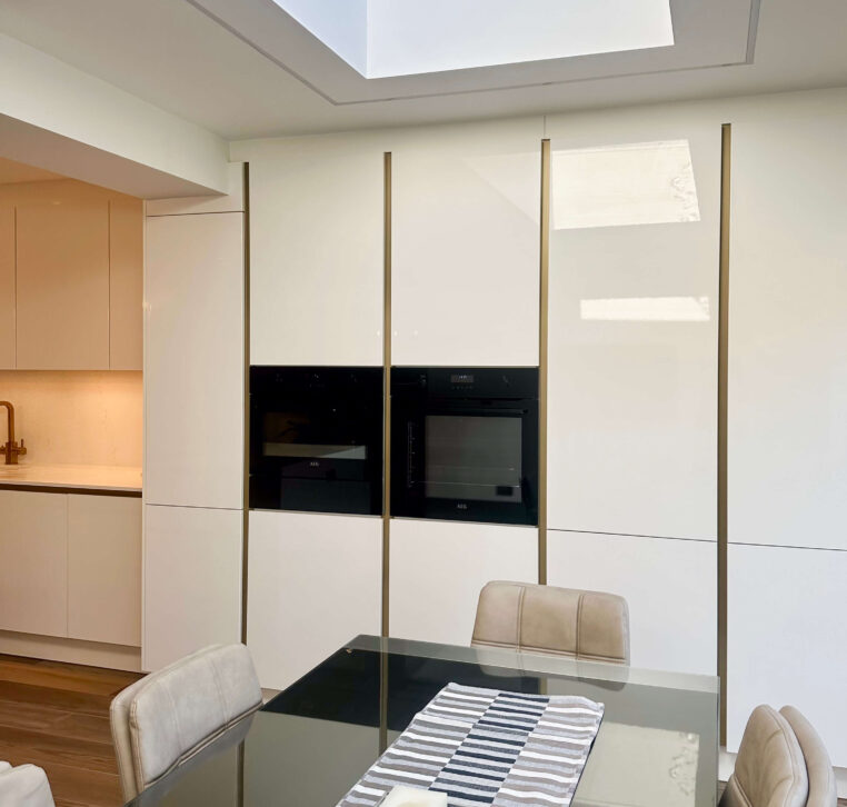 Modern kitchen with a glass dining table, beige upholstered chairs, and a skylight allowing natural light to brighten the space