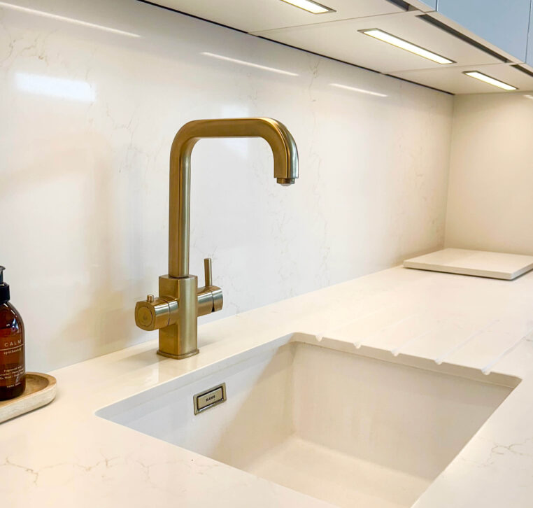 Close-up of a modern kitchen sink with a stylish golden faucet and illuminated under-cabinet lighting