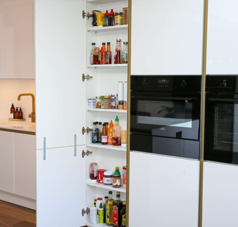 A sleek, modern kitchen pantry with open shelves filled with sauces, spices, and condiments, alongside built-in ovens.