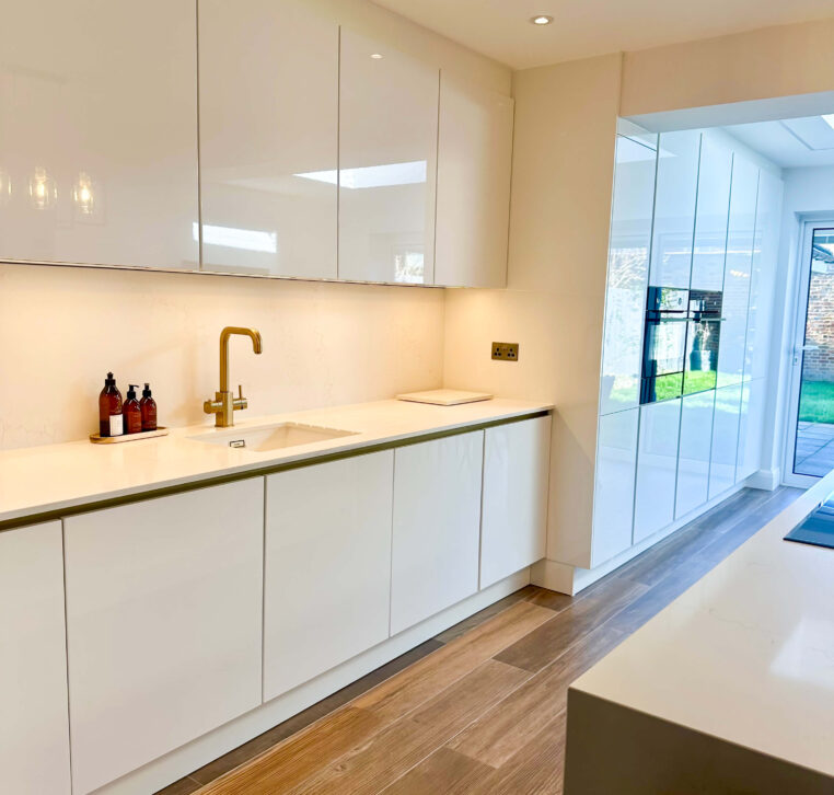 Modern white kitchen with minimalist design, including a sink area with golden faucet and ample storage space