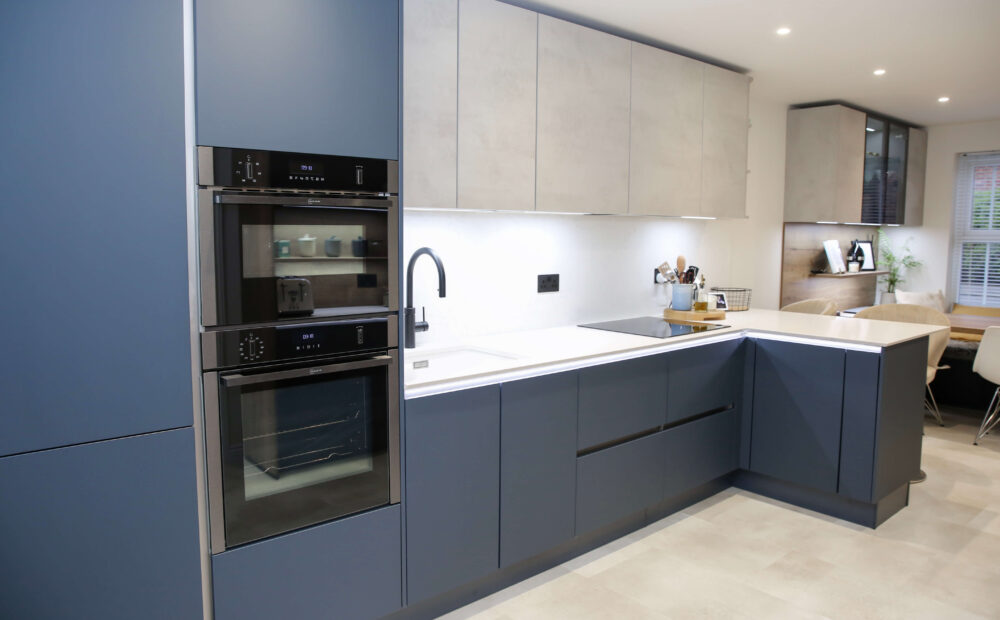 Full view of a modern L-shaped kitchen with navy blue cabinetry, double ovens, and a stylish breakfast bar