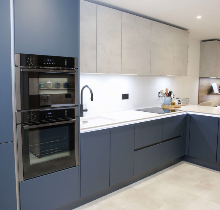 Full view of a modern L-shaped kitchen with navy blue cabinetry, double ovens, and a stylish breakfast bar