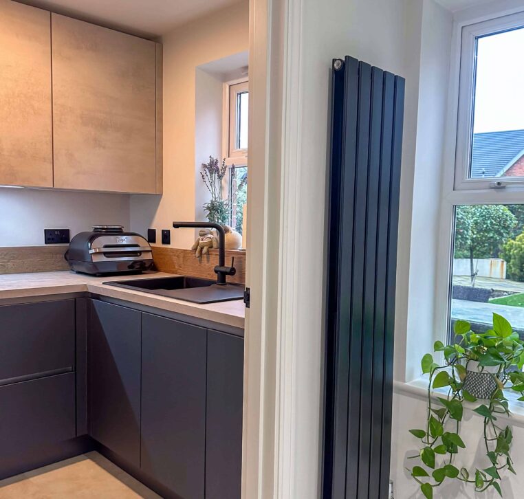 Compact yet stylish utility room with dark blue cabinetry, a black sink, and a tall radiator next to a large window with plants