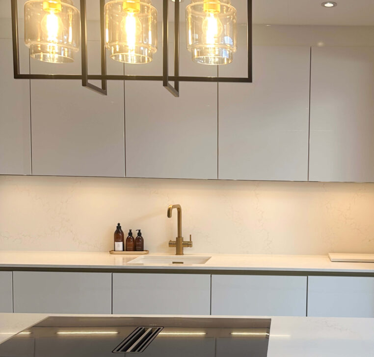 Close-up of industrial-style pendant lighting over a kitchen island, with clean white cabinetry and modern appliances