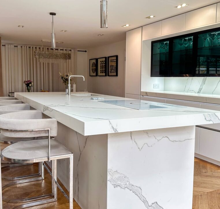 A high-end kitchen featuring a marble-clad island with seating, dark glass cabinets, and soft LED lighting.