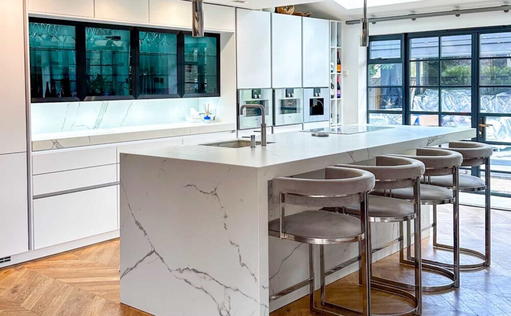 A modern kitchen with a striking marble island, chevron-patterned wooden flooring, and elegant bar stools.