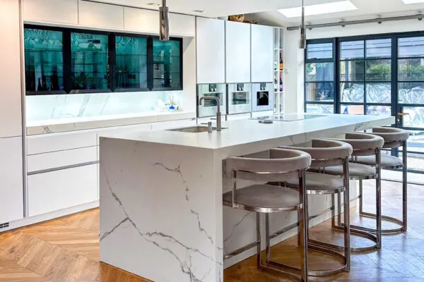 Luxury White Marble Kitchen with Waterfall Island, Chevron Wood Flooring, and Glass Cabinets