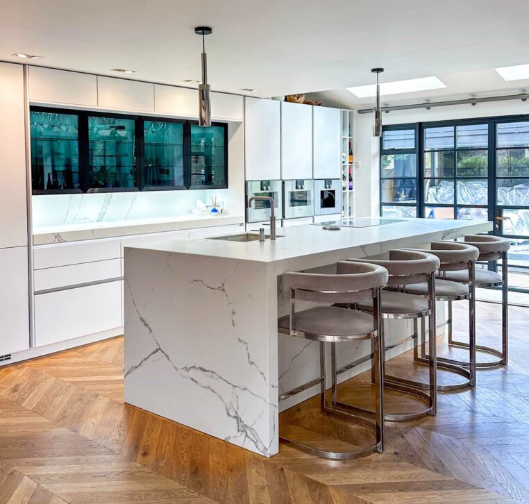 A modern kitchen with a striking marble island, chevron-patterned wooden flooring, and elegant bar stools.