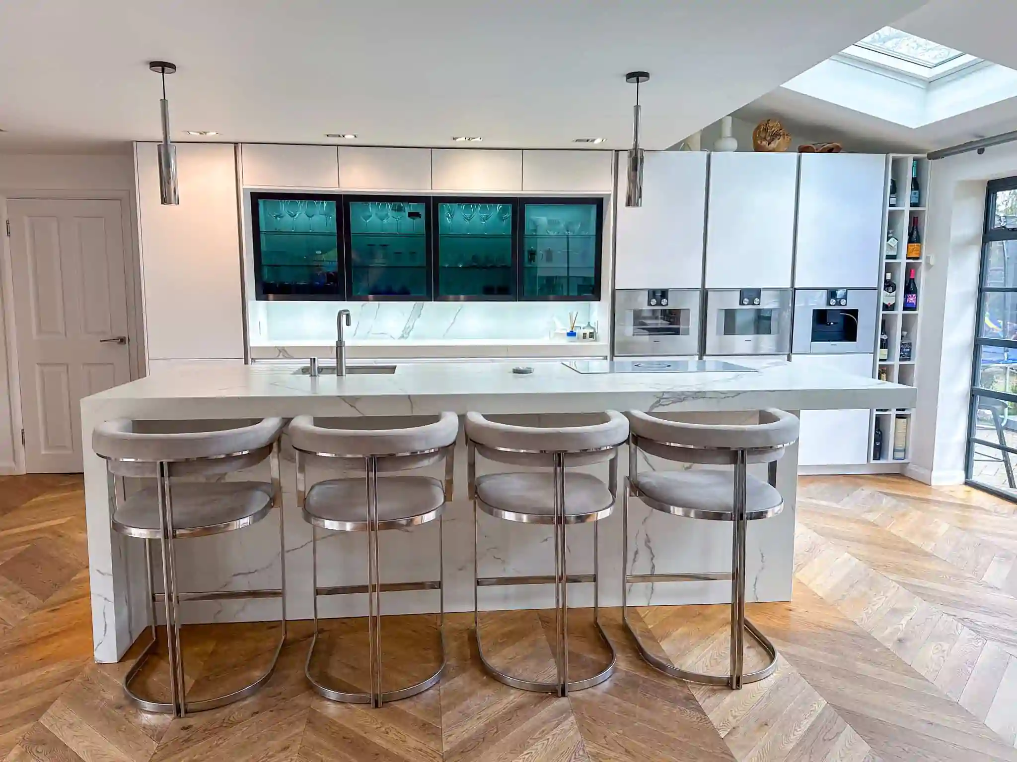 A high-end kitchen featuring a marble waterfall island with sleek bar stools and built-in appliances.