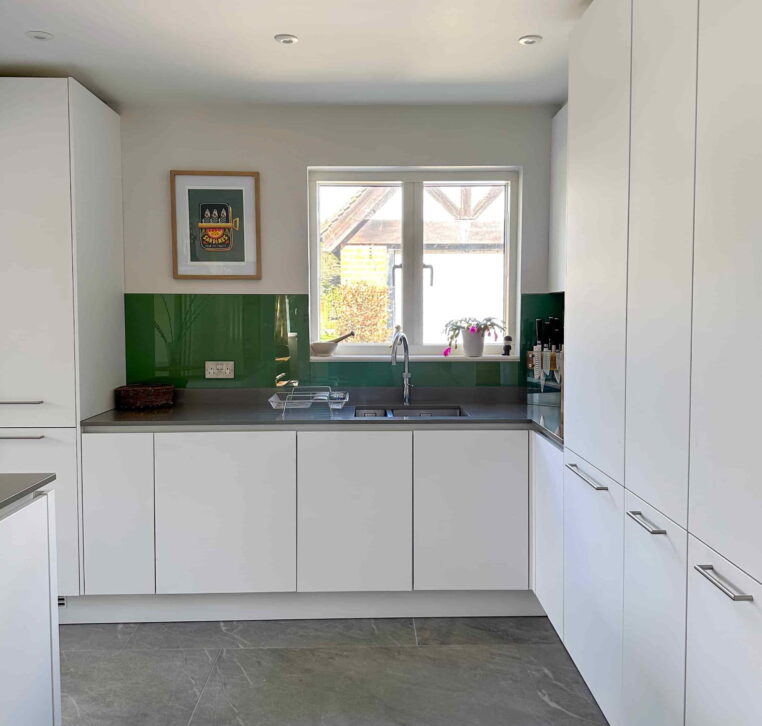 A modern kitchen with a grey countertop island, light fabric bar stools, and dark grey tiled flooring.