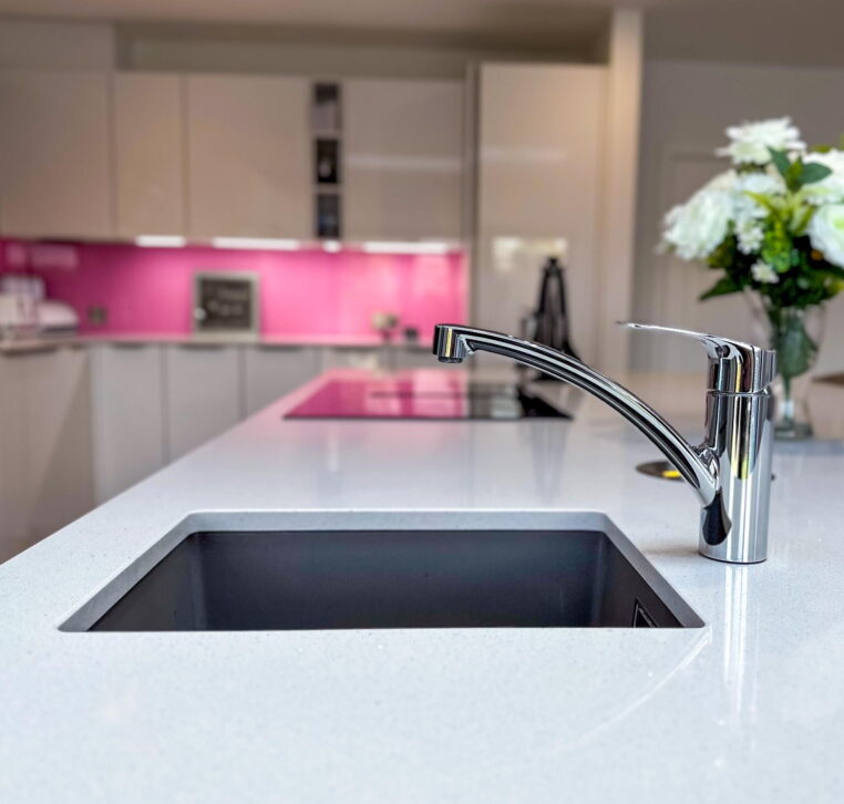 Modern kitchen with white cabinets, pink backsplash, decorative flowers, and integrated appliances.