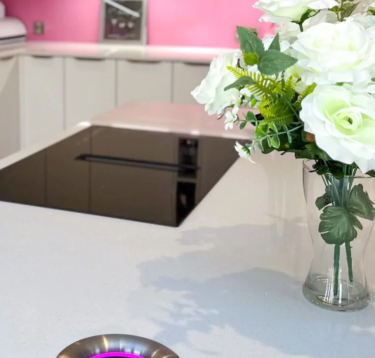 Close-up of modern kitchen island with black induction hob and a vase of white flowers on white countertop.