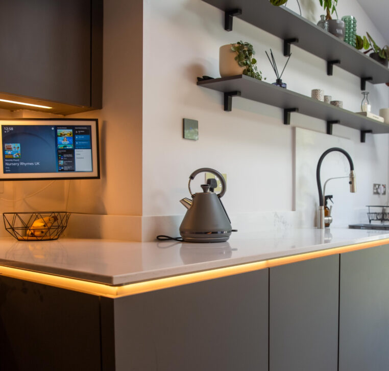 Close-up of kitchen worktop with warm under-cabinet lighting and decorative wall-mounted shelves.