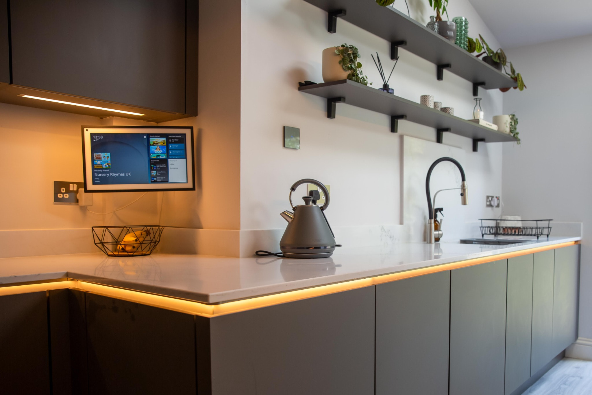 Close-up of kitchen worktop with warm under-cabinet lighting and decorative wall-mounted shelves.