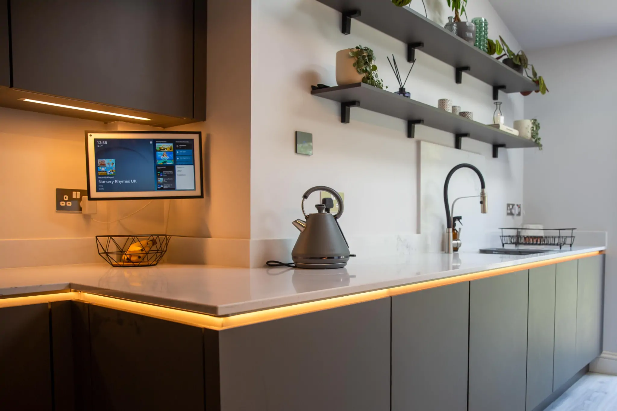 Close-up of kitchen worktop with warm under-cabinet lighting and decorative wall-mounted shelves.