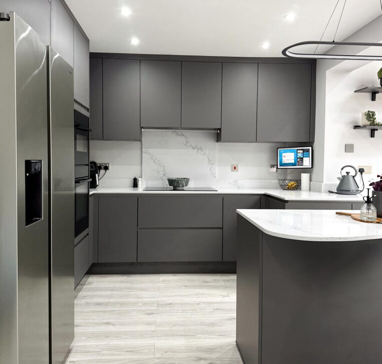 Open-plan grey kitchen with breakfast bar, green velvet stools, and pendant lighting.