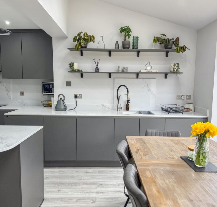 U-shaped grey kitchen featuring handleless cabinets, integrated appliances, and a white worktop.