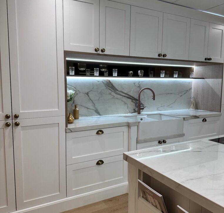 Luxury white kitchen featuring a marble splashback, under-cabinet lighting, and a copper faucet.