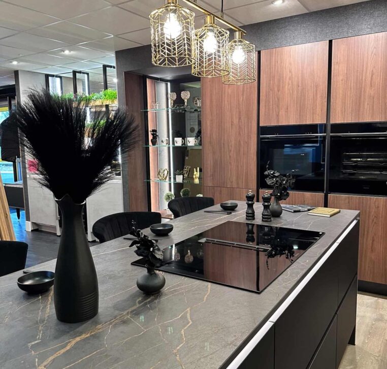 Modern black kitchen with golden light fixtures, a marble countertop, and a sleek design.