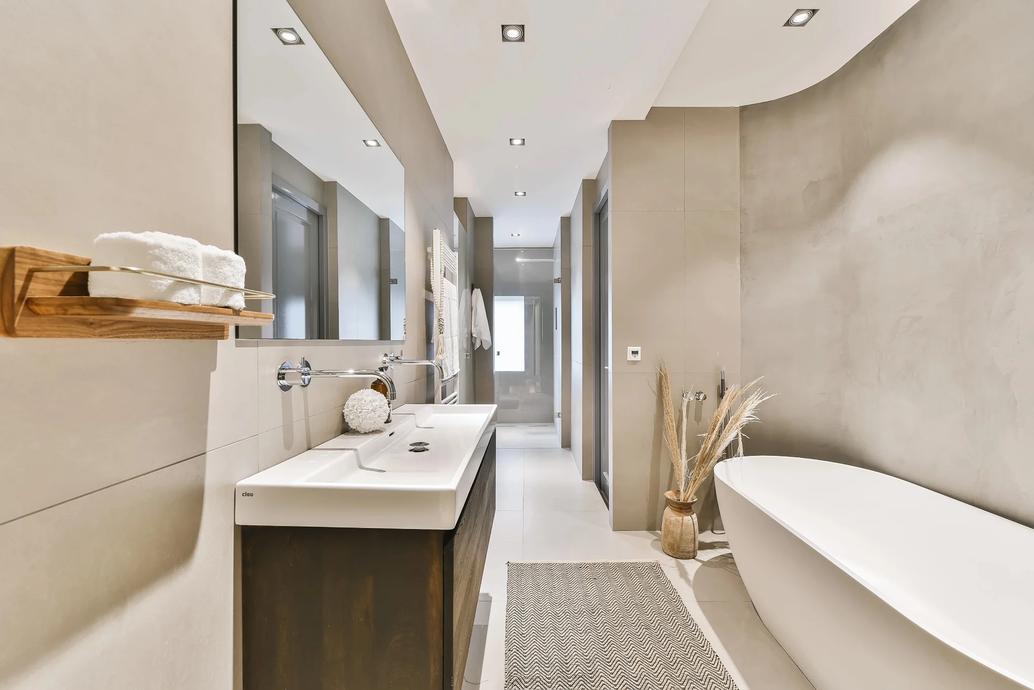 A bathroom with beige tiles, a large rectangular mirror above a sink, and a freestanding bathtub.