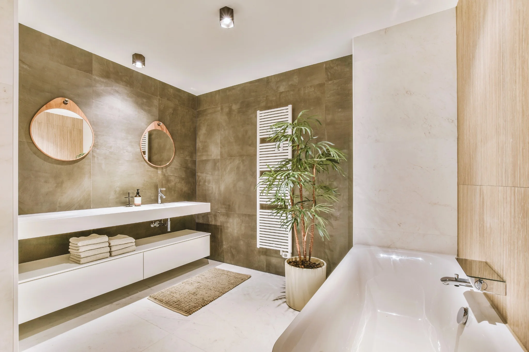 A contemporary bathroom with dark brown ceramic tiles, a white modern sink with a sleek mirror above. The space is complemented by a small towel rack and a decorative plant.