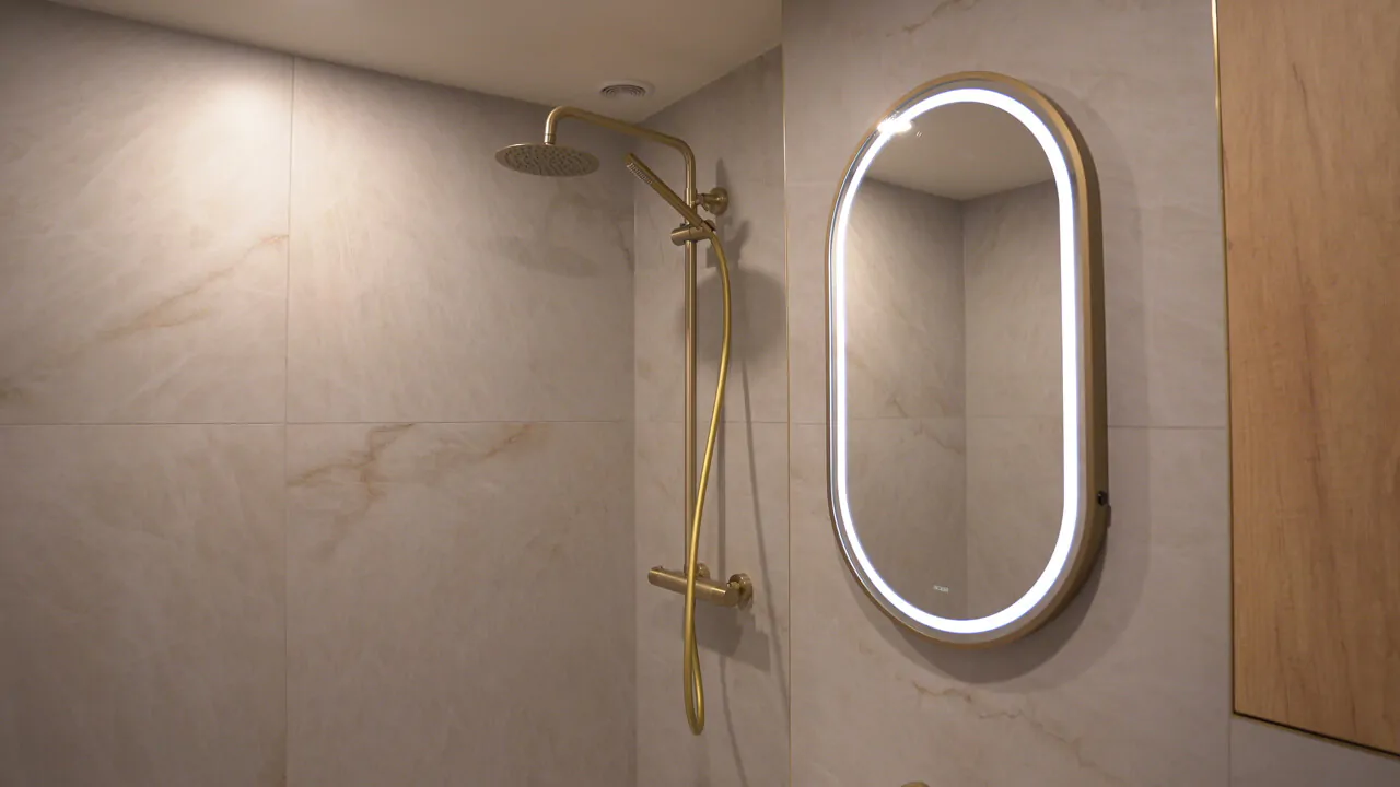 Bathroom view showing the coordination between the brushed gold shower system and the oval LED mirror.