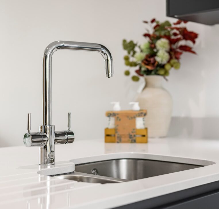 Close-up of chrome kitchen tap with flower vase in background