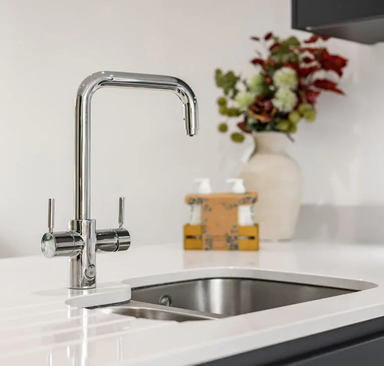 Close-up of chrome kitchen tap with flower vase in background