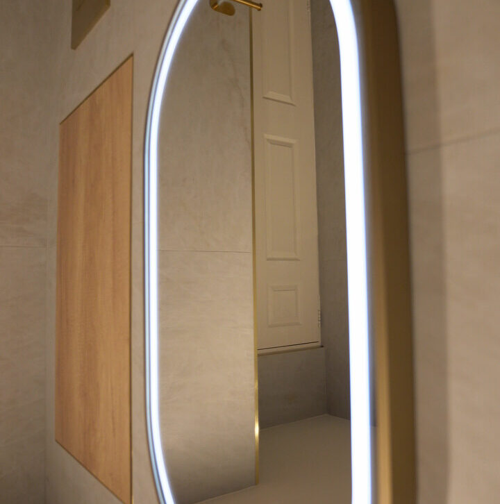 Side view of a glowing LED oval mirror reflecting a white paneled door in a luxury bathroom.