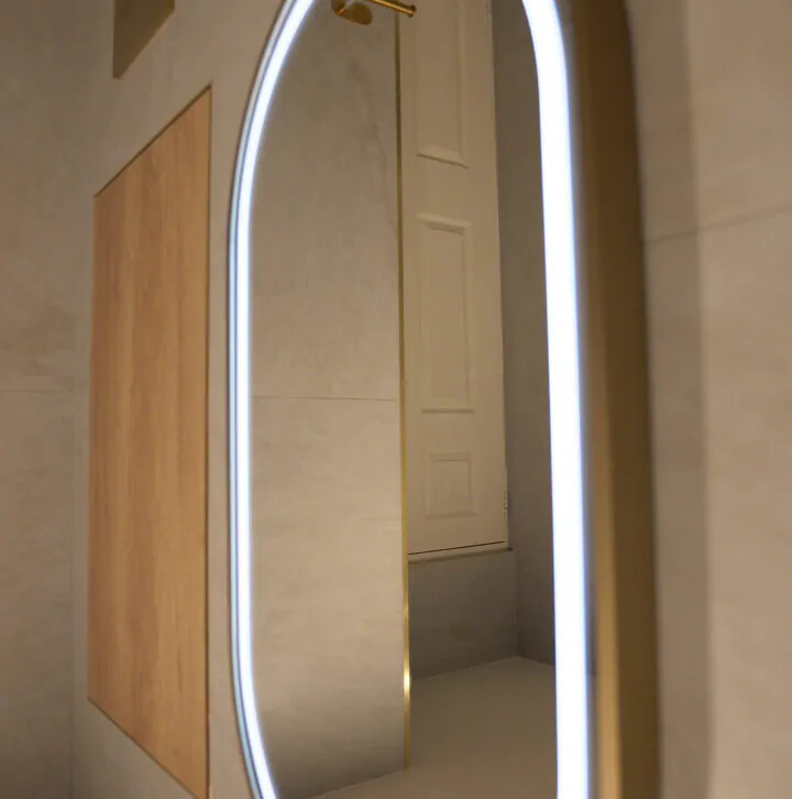 Side view of a glowing LED oval mirror reflecting a white paneled door in a luxury bathroom.