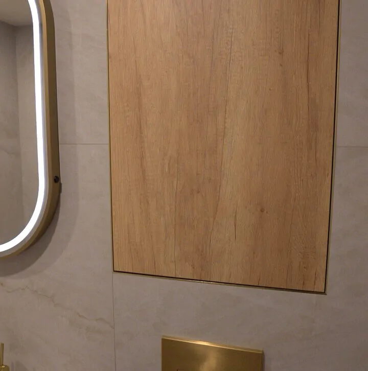 Recessed wood-effect wall paneling above a brushed gold flush plate in a modern bathroom renovation.