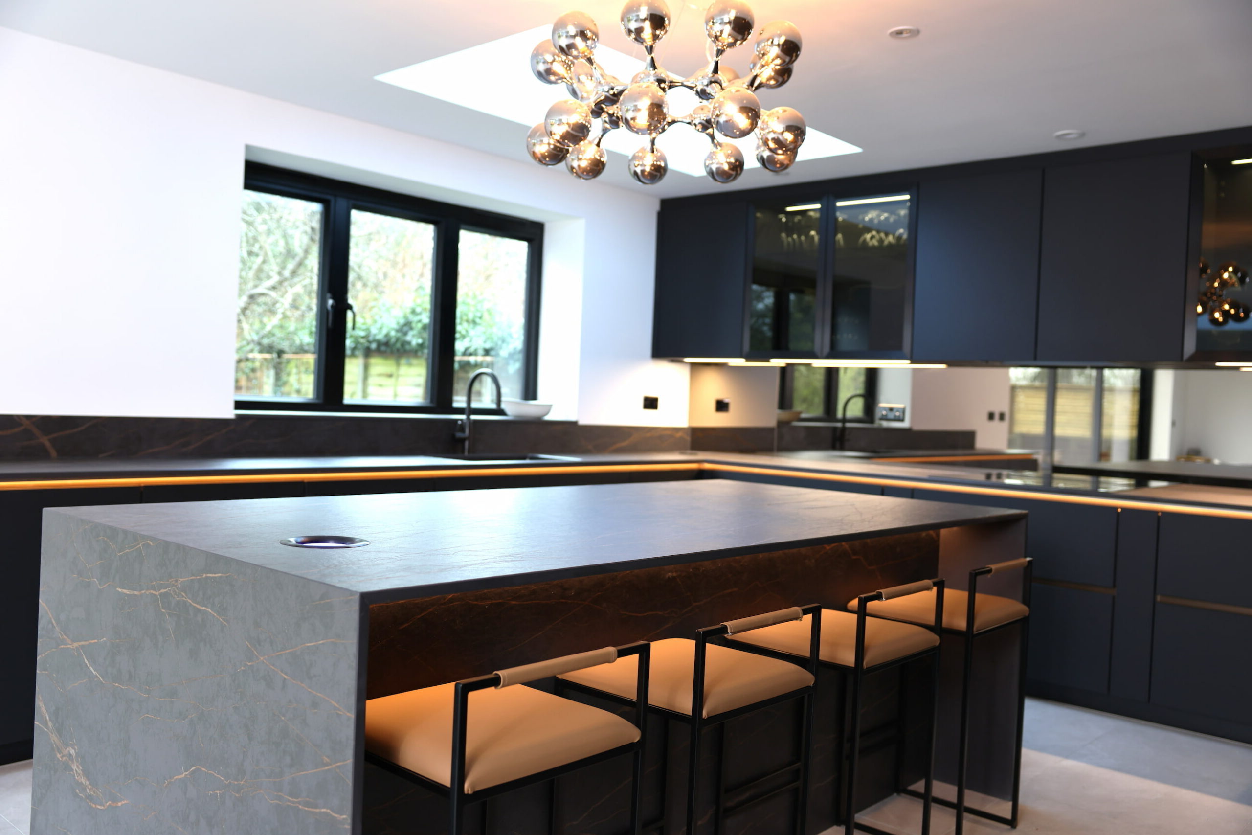 Kitchen island with bar seating, modern lighting and dark cabinetry detail