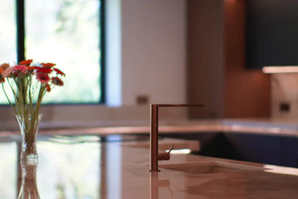 Modern kitchen featuring a marble countertop with copper tap and fresh flowers, designed and installed by MAS Collection.