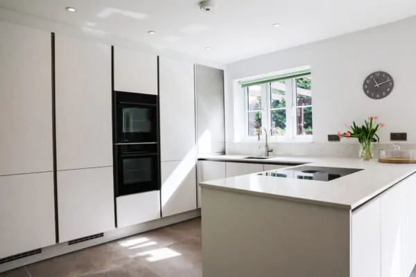 White handleless kitchen with large island-style worktop, integrated hob, built-in ovens and garden views